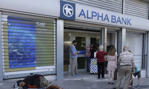 People stand in a queue to use an ATM of a bank as a person begs for alms, in Athens, Monday, July ...