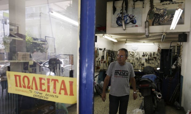 Mechanic Giorgos Prasinoudis steps out of his closed motorcycle repair shop, as a ‘For Sale&#...
