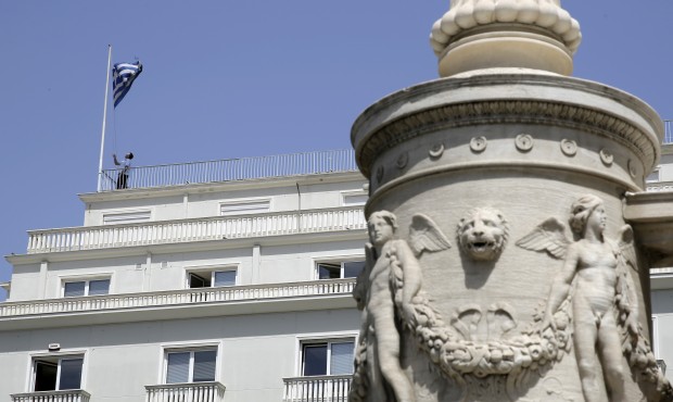 A man lowers the Greek flag on the roof of an office block, as an ornamental lamppost base from the...