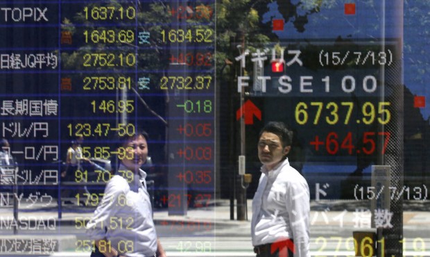 People are reflected on an electric board as they watch financial markets indexes in Tokyo Tuesday,...