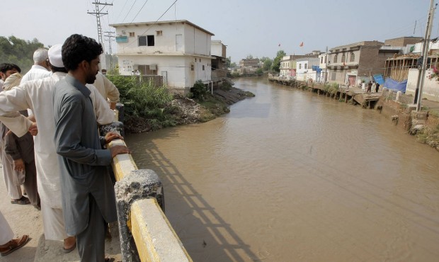 Pakistani villagers watch a stream over flowing due to rain in Peshawar, Pakistan, Friday, July 24,...