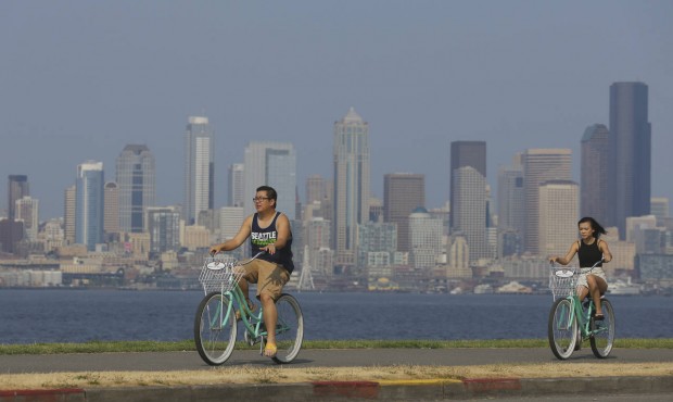 Cyclists ride on a sidewalk in West Seattle as downtown Seattle is cloaked in haze behind them, Thu...