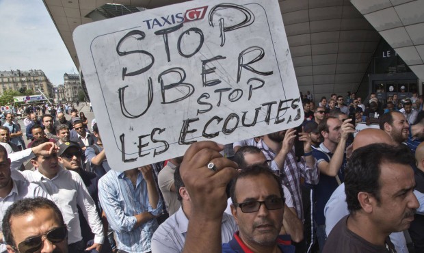 FILE – This Thursday, June 25, 2015 file photo shows a striking taxi driver holding a placard...