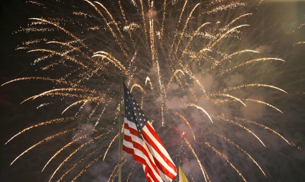 FILE – In this July 4, 2015 file photo, fireworks explode behind a United States flag during ...